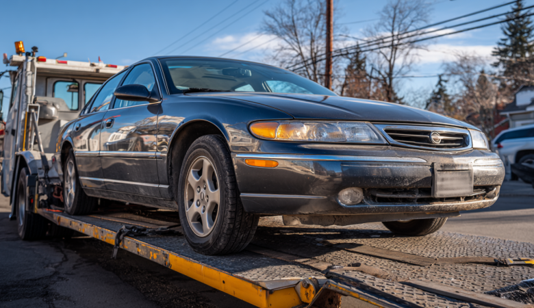 A non-running car sitting on a flatbed tow truck.